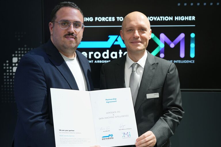 Partnership Agreement Aerodata-DMI: Pau Garcia and Thomas Krüger hold the signed Agreement and smile at the camera.